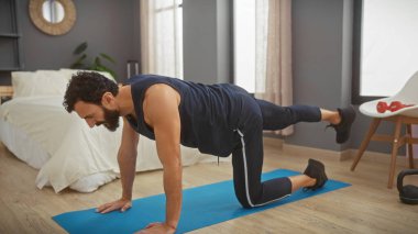 Sakallı bir adam yatak odasında egzersiz yapıyor. Spor salonu, yaşam tarzı ve evcimenliği gösteriyor..