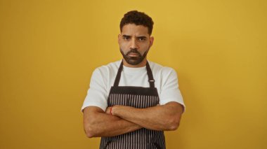 Sarı arka planda önlük takan sakallı çekici genç adam kollarını kavuşturmuş ciddi görünüyor.