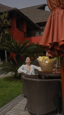 Kumral bir kadın lüks bir tatil köyünde dinleniyor, gözleri kapalı gülümsüyor. Etrafı tropik yeşilliklerle çevrili..