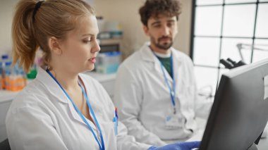 Laboratuvar önlüklü bir kadın ve erkek, parlak, modern bir laboratuvar ortamında bir bilgisayar ekranını inceliyor..