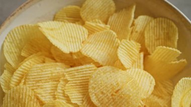 Closeup of yellow crispy potato chips in a bowl, showcasing their texture and freshness. clipart