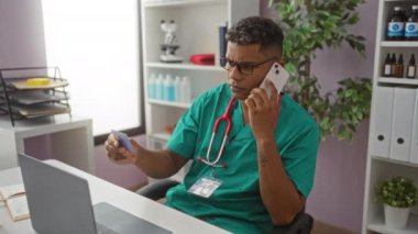 Hastane işyerindeki yeşil önlüklü İspanyol adam akıllı telefondan konuşuyor ve kredi kartını inceliyor..