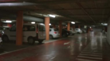 Arka planda çözünmüş arabalar ve loş ışıklandırma olan kapalı bir park alanı karamsar bir atmosfer yaratıyor.