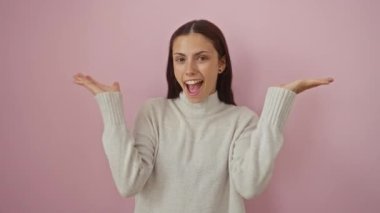 Soyutlanmış pembe bir arka planda poz veren genç bir kadın neşeli bir ifadeyle, mutluluk ve heyecan taşıyor.