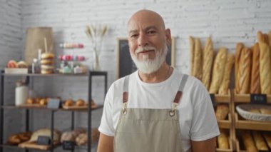 Fırında gülümseyen sakallı, kır saçlı adam. Etrafı ekmek ve hamur işleriyle çevrili.