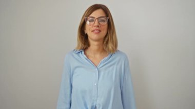 Sarışın, gözlüklü genç bir kadın gözlerini kapayarak gülümsüyor. İzole edilmiş beyaz arka planda şaşkınlık içinde. Şaşırmanın ve sevincin neşeli ifadesi.