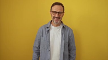 İspanyol adam, orta yaşlı, gözlük takıyor, ayakta duruyor, gülümsüyor olumlu onay işareti gösteriyor, mükemmel izole edilmiş sarı arka plan.