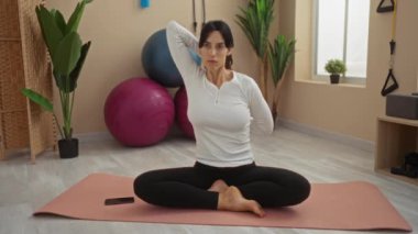 Kadın spor salonunda pembe paspasla esniyor. Büyük egzersiz topları içeride bitkiler ve sakin bir ortam.