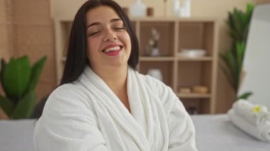 Rahat beyaz bir bornozla kaplıcada rahatlatıcı spa dekoru ve yeşilliklerle çevrili bir kadın, sakin ve kapalı bir sağlık ortamını ön plana çıkarıyor..