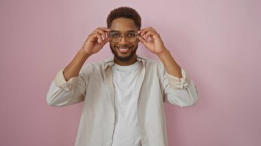 Yakışıklı, gülümseyen ve gözlükleri ayarlayan genç bir adam. İki eli de soyutlanmış pembe bir arka plan üzerinde.
