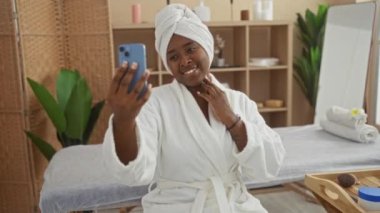 Kapalı bir sağlık merkezinde telefonuyla selfie çekerken kafasında sabahlık ve havlu olan genç bir kadın spa 'da dinleniyor.