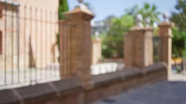 Açık hava kentsel ortamının bulanık arkaplanı. Odaklanamayan tuğla çit, yeşillik ve güneş ışığı bir bokeh etkisi yaratıyor.