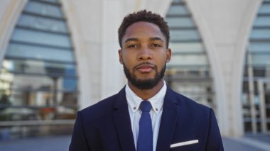 Takım elbiseli genç bir adam şehrin bir caddesinde duruyor, kendine güven ve profesyonellik yayıyor..