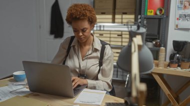 Focused african woman detective working on a case in a busy police department office. clipart