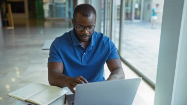 Ofiste dizüstü bilgisayarı ve not defteriyle çalışan yakışıklı siyahi adam daktiloya odaklanmış.