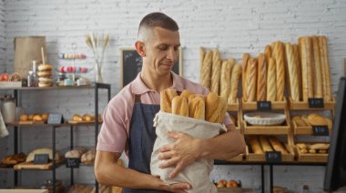 Pastanede elinde ekmek ve pastane rafları olan bir torba ekmek tutan genç adam.