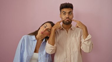 Kadın ve erkek pembe arka planda birlikte komik suratlar yapıyor, neşeli ve sevgi dolu bir ilişki sergiliyorlar.