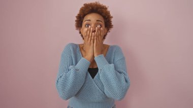 Şaşırmış bir Afrikalı Amerikalı kadın ellerini pembe bir arka plana sürerek ağzını kapatıyor..