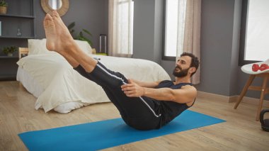 Yatak odasında yoga minderi üzerinde egzersiz yapan sakallı bir adam pilates yaparken odaklanmış ve kararlı..