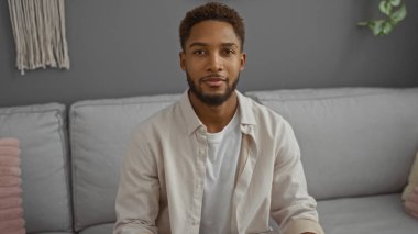 Yakışıklı, Afro-Amerikalı bir adam modern bir oturma odasında sessizce oturuyor.