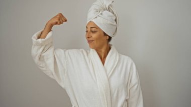 Kafasında havluyla bornoz giymiş beyaz bir arka plana yaslanmış, kendine güven ve güç saçan bir kadın.