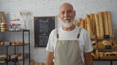 Bir pastanede çalışan ve arka planda çeşitli ekmek ürünleri olan bir adam müşterilere sıcak bir konukseverlik ve hizmet sunuyor.
