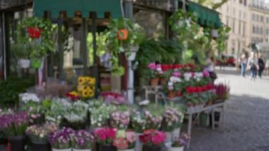 Çiçekler arka planda bulanık insanlarla dolu kalabalık bir caddedeki açık hava büfesinde sergileniyor, güneşli bir günde canlı bir çiçekçi dükkânı yakalıyorlar..