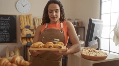 Pastanede önlük takan genç bir kadın sıcak bir iç mekanda ekmek ve kurabiyelerle tezgahın yanında dururken...