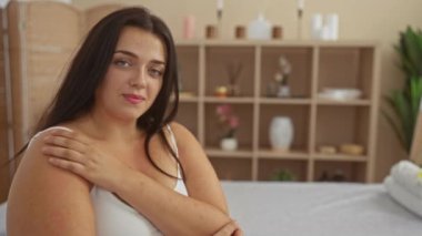 Sakin bir atmosferi olan, sakin bir spa odasında dinlenen bir kadın, rahatlatıcı bir dekor ve temiz bir iç mekan ile çevrili, doğal güzelliğini ve kıvrımlı, büyük beden figürlerini sergiliyor.