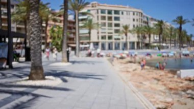 Açık deniz yolu, insanların plaj ağaçları ve açık mavi gökyüzünün altındaki binalarla bulanık..