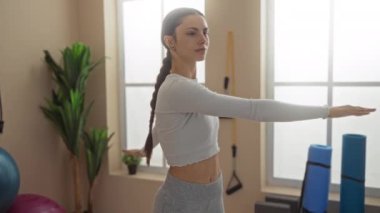 Spor salonunda iç mimari ve spor aletleriyle egzersiz yapan, spor kıyafetleri giyen, odaklanan ve kollarını esneten bir kadın..