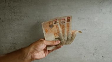 İngiliz sterlinli banknotları beton duvara dayayan adam, para birimini sergilerken el ve parmaklarını açıkça gösteriyor.