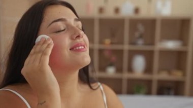 Kapalı bir güzellik merkezinde yüzünü pamukla temizlerken ve kıvrımlı ve güzel vücudunu sergileyerek rahatlatıcı bir spa gösterisinden zevk alan bir kadın..