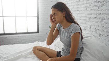 Beyaz duvarları ve geniş penceresi olan bir odada yatağında oturan bir kadın acı hisseder.