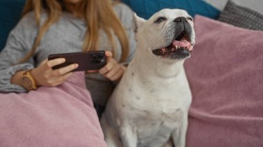 Genç bir kadın evindeki oturma odasında akıllı telefon kullanırken evcil köpeğiyle evde dinleniyor..