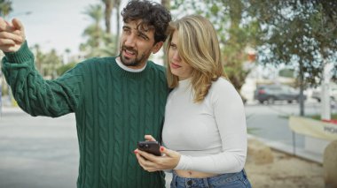 Güneşli bir şehir sokağında akıllı telefon kullanan bir erkek ve kadın aşk, bağlantı ve kentsellik temaları çağrıştırıyor..