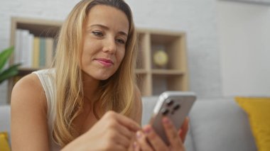 Modern bir oturma odasında akıllı telefon kullanan beyaz bir kadın.