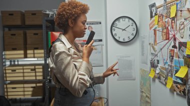 African american woman detective examines evidence in a police station's investigation room. clipart