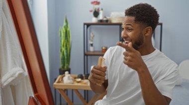 Genç bir adam, elinde tarak olan bir spa salonundaki yansımasını gösteriyor. Etrafı güzellik dekoruyla çevrili..