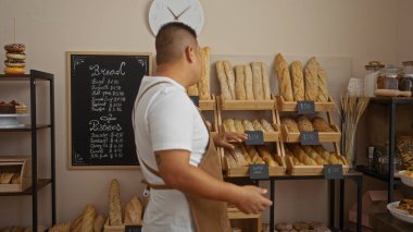 Genç bir İspanyol pastanede karatahta menüsündeki ahşap raflarda ekmek düzenliyor.