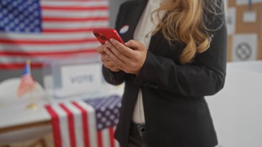 Amerikan üniversitesi seçim merkezinde bayrakla süslenmiş genç bir kadın telefonunu kontrol ediyor..
