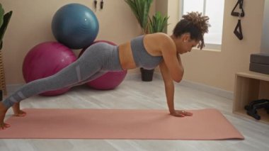 Arka planda spor topları olan bir yoga minderinde egzersiz yapan bir kadın atletik yeteneklerini ve adanmışlığını sergiliyor.