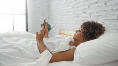 Yatakta uzanmış bir kadın şok olmuş bir ifadeyle telefonuna bakıyor. Etrafı modern yatak odası dekorasyonuyla çevrili. Pencereden içeri güneş ışığı giriyor..