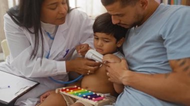 Çocuk doktoru, tıbbi danışmanlık sırasında evde babasıyla birlikte çocuğu muayene ediyor.