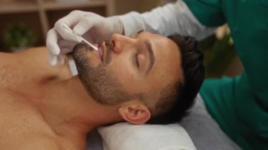 Man receiving lip treatment from therapist in a spa room, highlighting wellness and beauty care in an indoor setting