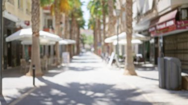 Beyaz şemsiyelerin altında oturma yerleri olan palmiye ağaçları ve kafelerle kaplı bir açık hava manzarası