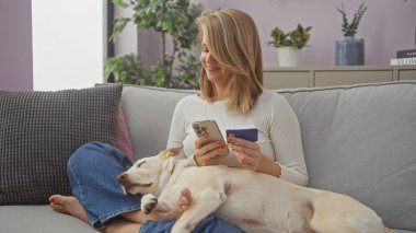 Kapalı bir koltukta uyuyan bir köpekle kredi kartı ve akıllı telefon tutan genç bir kadın.