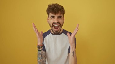 Sakallı ve dövmeli yakışıklı, heyecanlı adam sarı duvara yaslanmış tezahürat yapıyor.