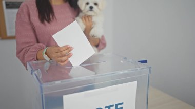 Genç bir İspanyol kadın evde oy verirken bichon köpeğini tutuyor.