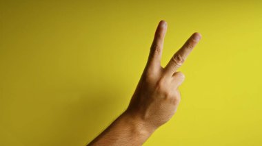 Man showing a victory hand gesture with two fingers on a yellow background, highlighting a positive and cheerful theme. clipart